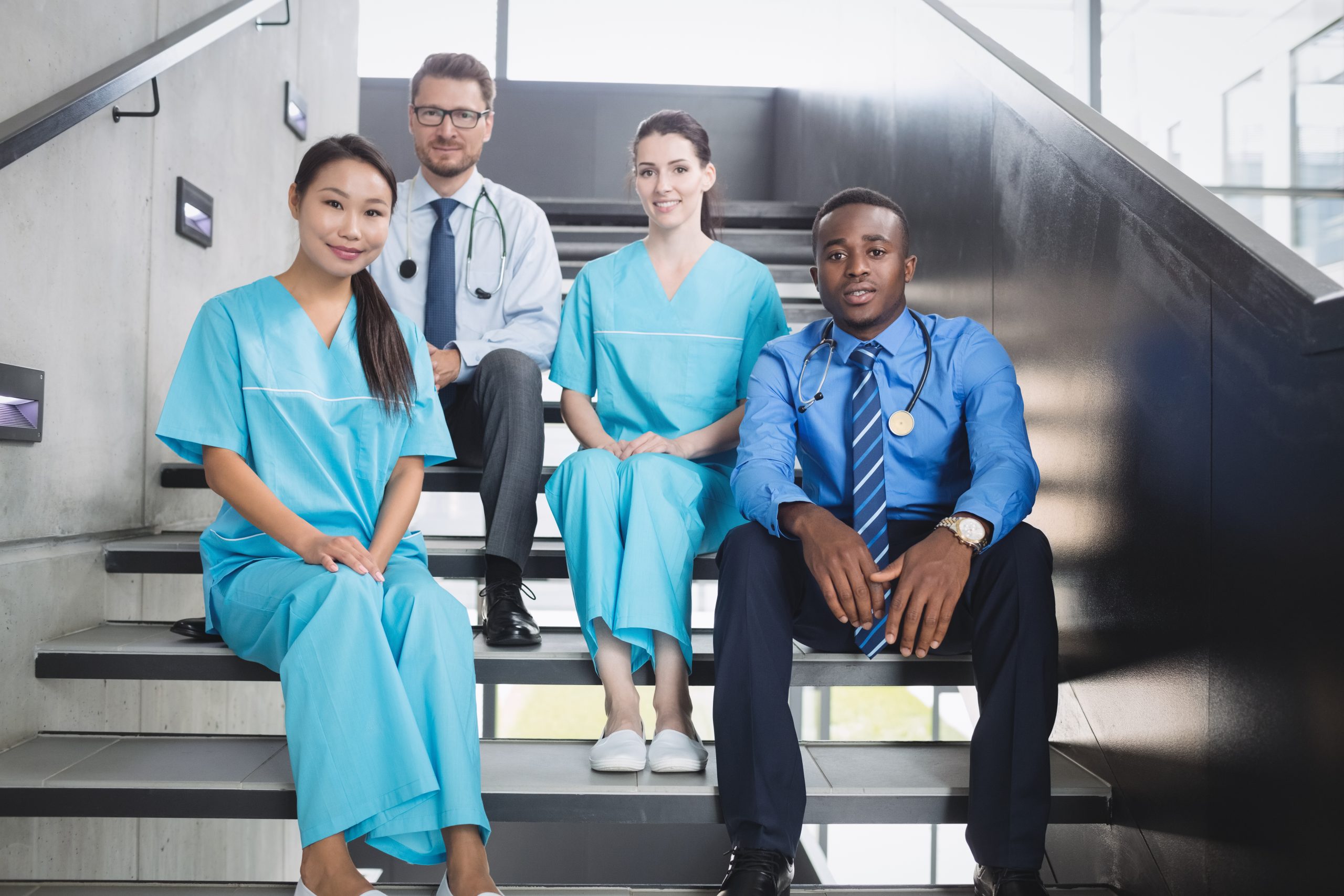 Portrait of smiling doctors and nurses sitting on staircase in hospital